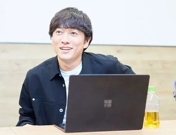 市原創吾がノートパソコンの前で談笑する様子。座っているが、身長の高そうな印象が伝わる。