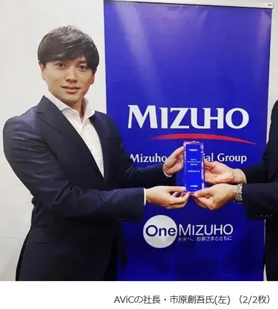 市原創吾がMizuhoのロゴの前で表彰を受ける姿。スーツ姿で身長が際立つ構図